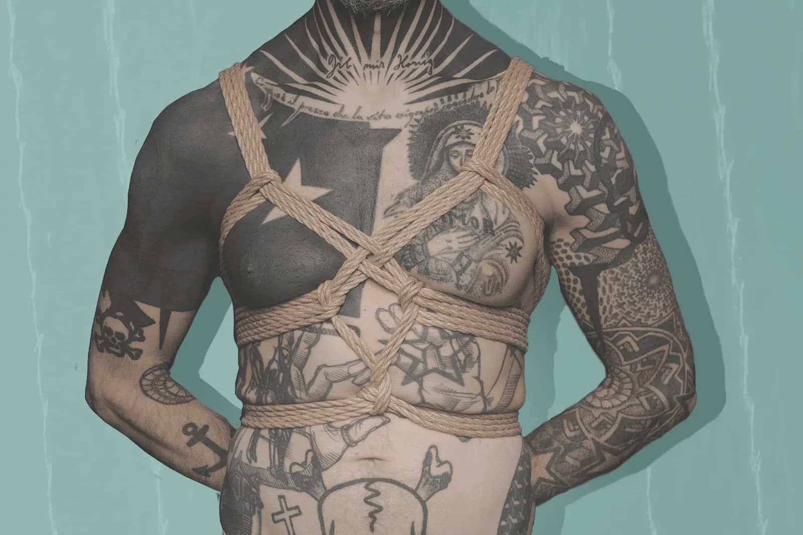 tattooed man in arms-free chest harness against a teal background.