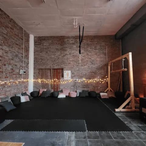A rope studio interior with brick walls, suspended equipment, cushions, and warm lighting.