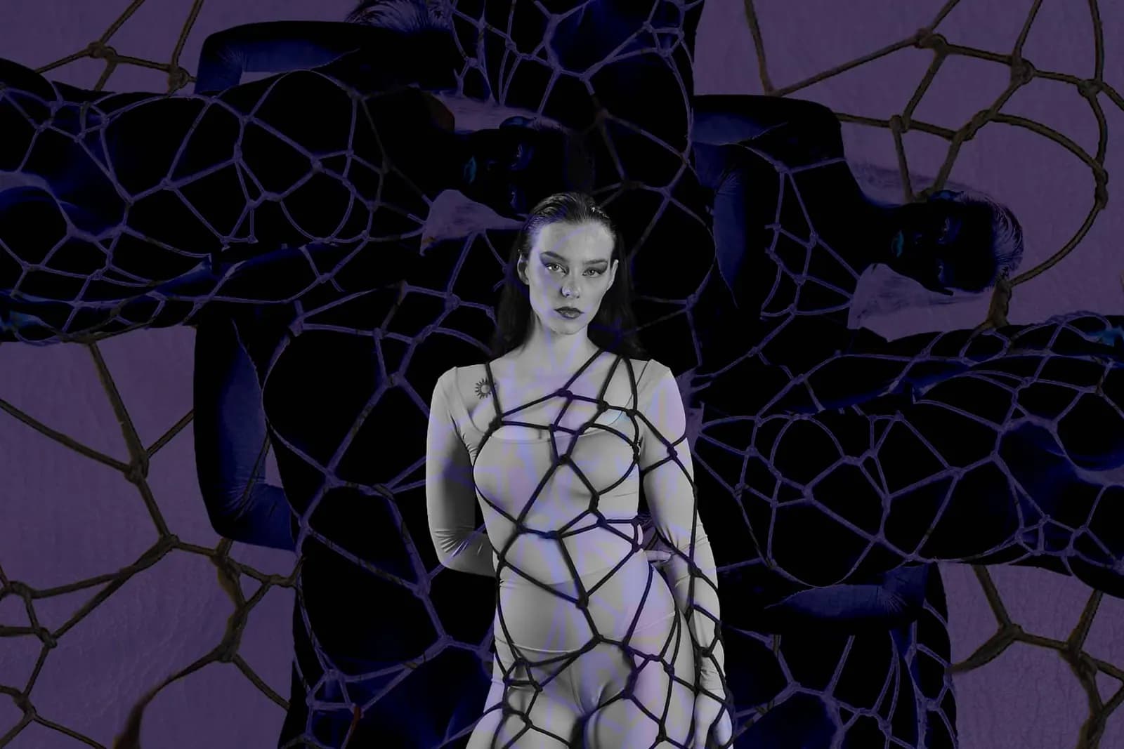 A woman in a shibari web harness stands against a dark, purple, web-like background.