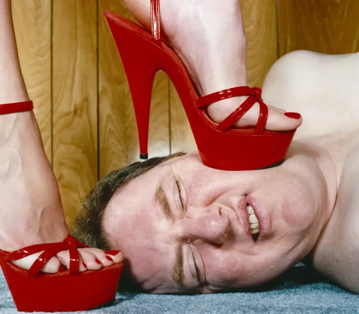 A person lying down beneath a pair of red high heels
