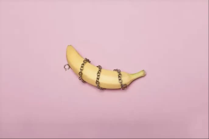 A banana wrapped in a fine chain against a pink backdrop