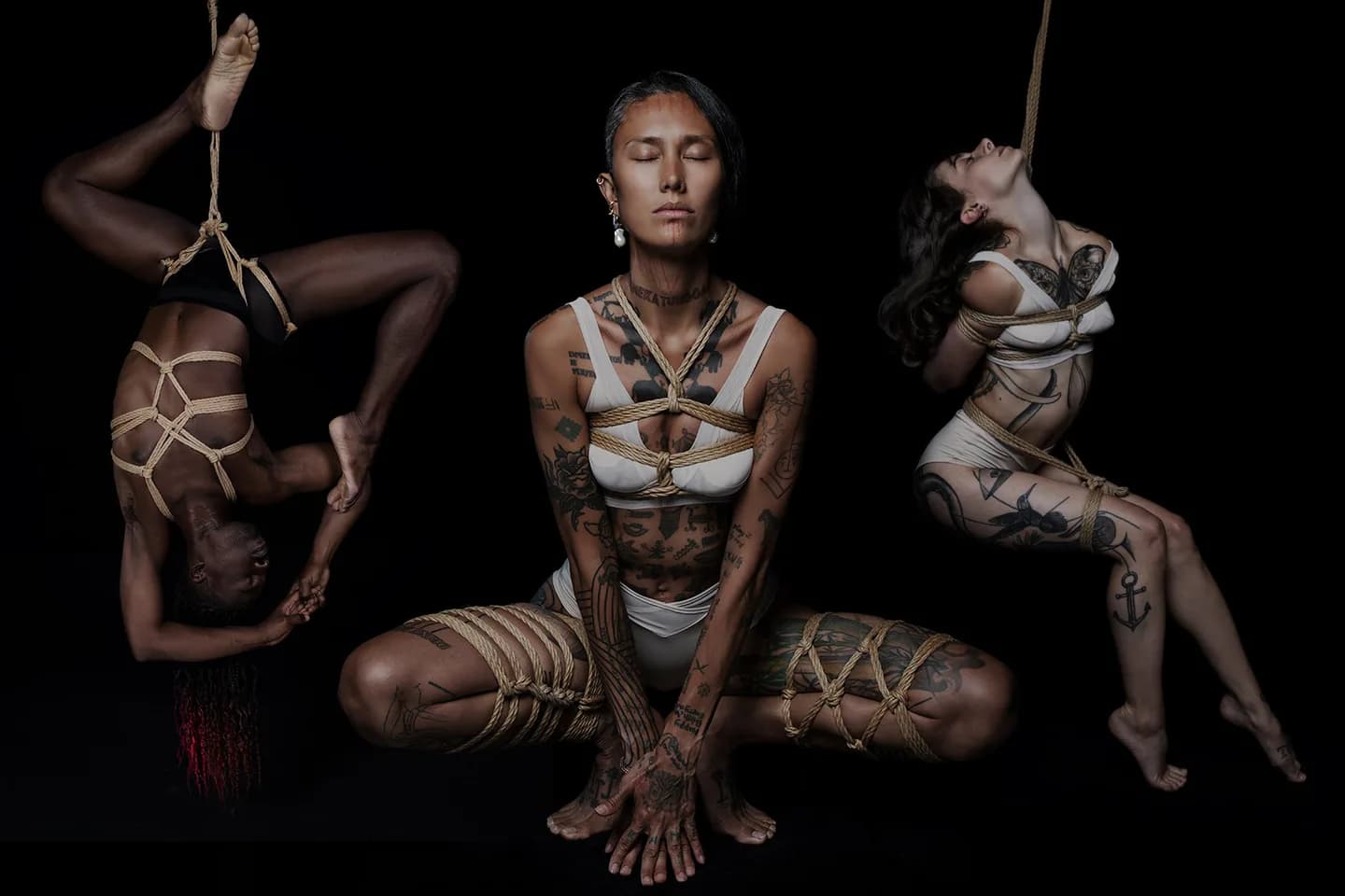 Three people in rope harnesses posing against a dark backdrop