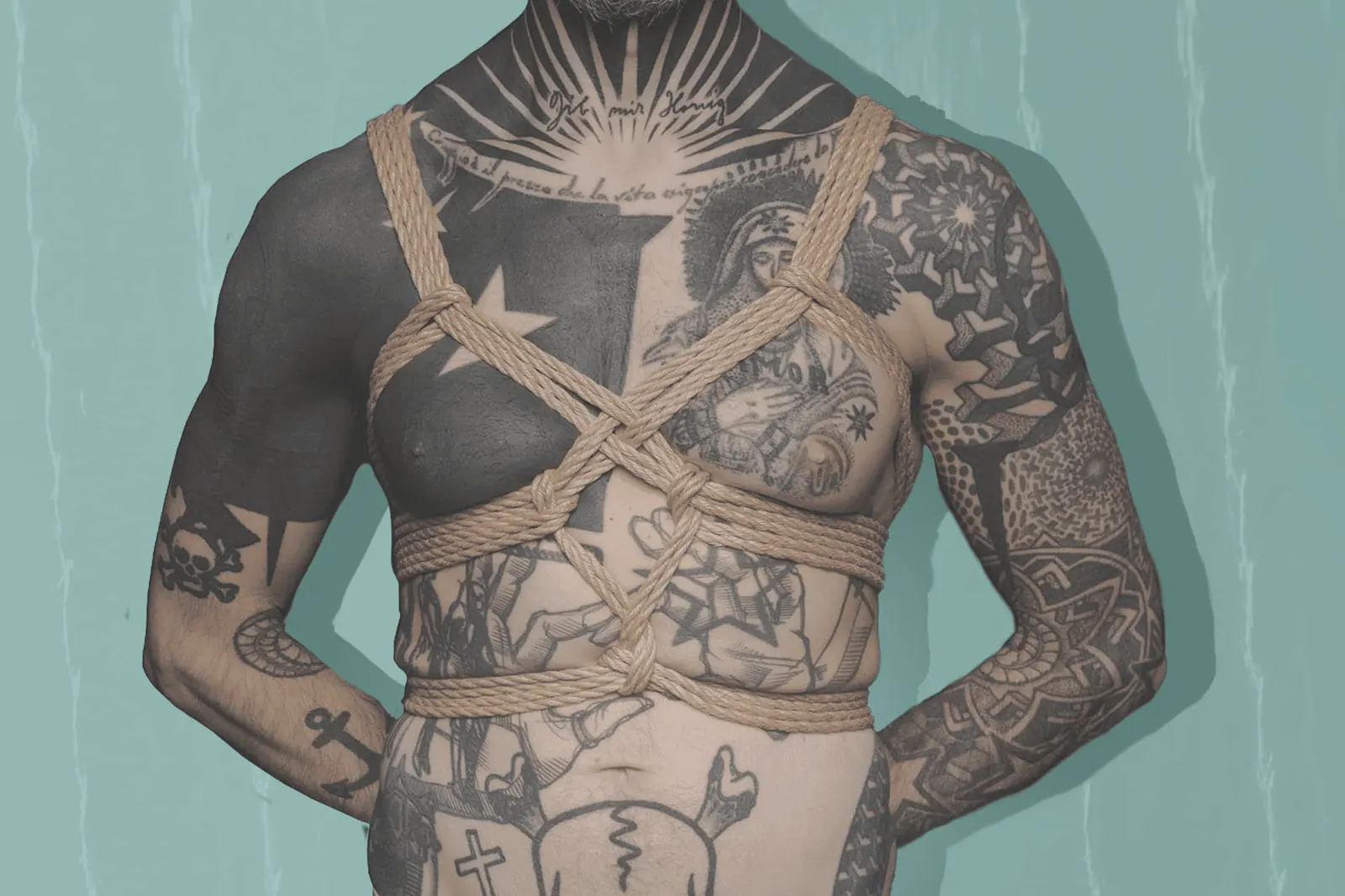 tattooed man in arms-free chest harness against a teal background.