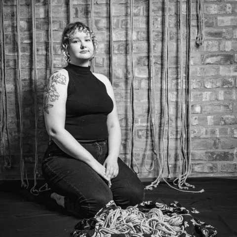 A person seated with coiled shibari ropes.