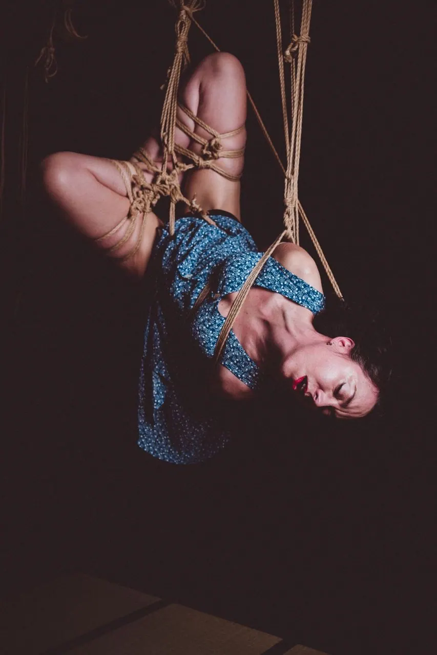 A person suspended vertically with natural jute rope.