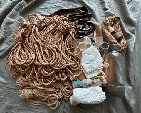 Flat lay of jute rope, carabiners, and bondage accessories on fabric.