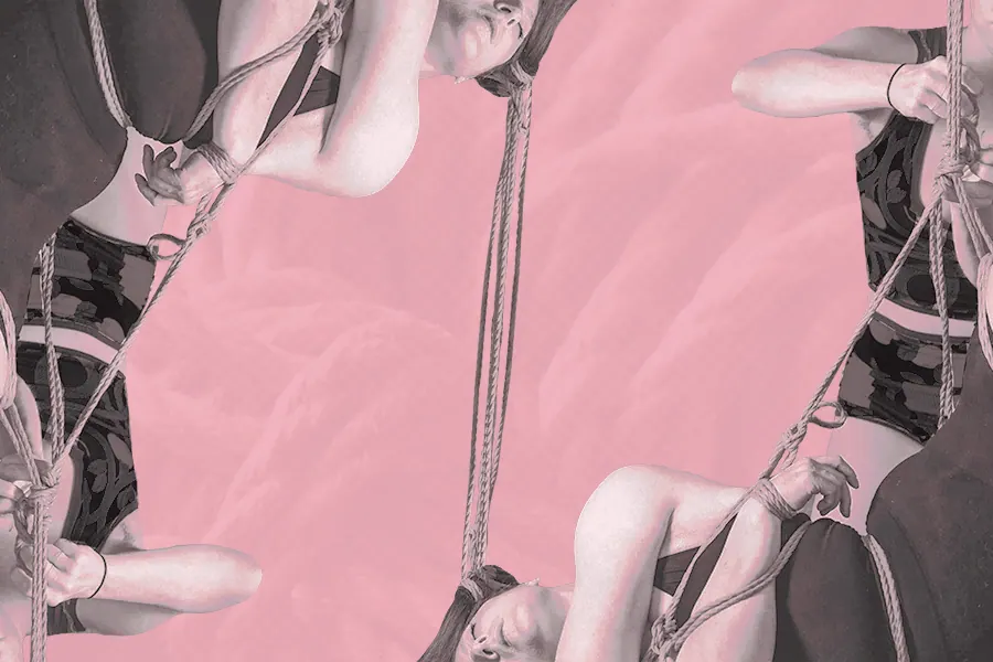 Close-up of hands holding rope around shoulders, lit in blue and magenta tones.