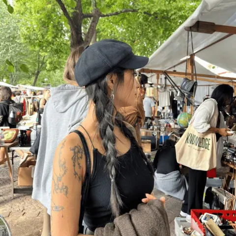 A person at an outdoor market or festival event wearing dark sleeveless top with visible tattoos.