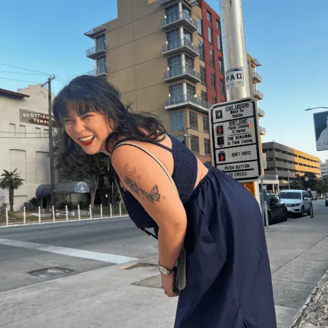 Person posing outdoors in an urban street setting with visible shoulder tattoo.