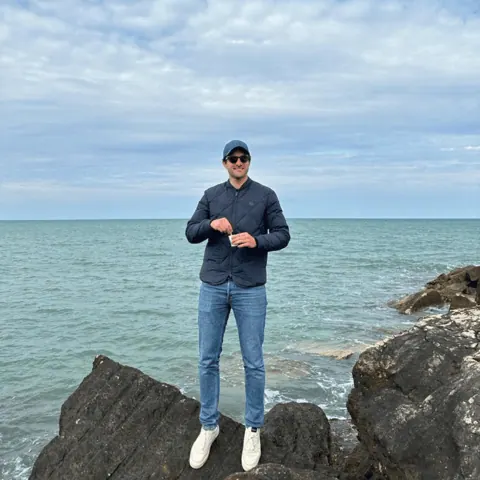 A person standing on coastal rocks beside the ocean on a clear day.