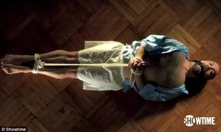 A character suspended by rope in a scene from television.