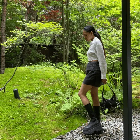 A person standing on a woodland path amid ferns and green trees.